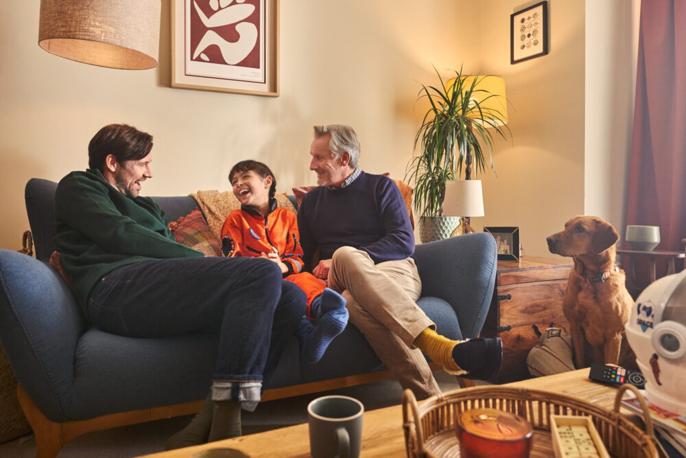 father grandfather and little girl sitting on a sofa with dog on the floor